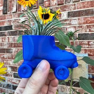 May include: A blue roller skate planter with a green air plant and yellow sunflowers. The planter is made of plastic and has four wheels.