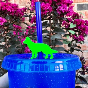 May include: A blue reusable cup with a glitter finish and a green dog silhouette on the lid. A blue straw is sticking out of the lid.