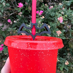 May include: A red reusable cup with a black bat straw topper. The cup has a glittery finish.