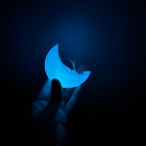 May include: A hand holds a glowing blue crescent moon-shaped object against a dark background.