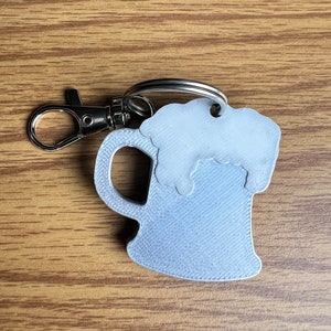 May include: A silver-colored metal keychain shaped like a beer mug with a foam top. The keychain has a silver-colored metal ring.