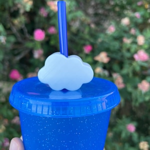May include: A blue glitter tumbler with a white cloud lid and a blue straw. The tumbler is perfect for holding cold beverages.