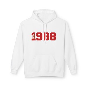 May include: White hoodie with a front pouch pocket. The garment displays the number "1938" in bold red block letters across the chest, with the letters "AOX" above the number 1938.