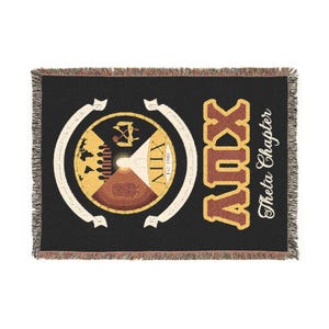 Könnte beinhalten: Schwarze gewebte Decke mit Fransen. Sie verfügt über ein kreisförmiges Emblem mit einem hell- und dunkelbraunen Design, dem Text "XIV" und "Est. 1988". Die Decke zeigt auch die Buchstaben "ADX" in Braun und Gold sowie die Worte "Theta Chapter".