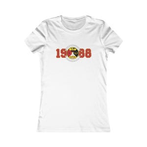 May include: White t-shirt with a crew neck. The shirt features a graphic with the numbers "1988" in red, and a circular emblem with a red, yellow, and black design. The text "ATX" is below the emblem.