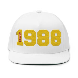 May include: A white flat-peak cap featuring the year "1988" embroidered in gold, with the Greek letters "ΛΠX" in red on the left. The cap has a structured crown and a flat peak.