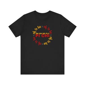 May include: Black t-shirt featuring a circular design in red, yellow, and white. The design includes the text "oh to be" and "AN OH SO FLY PI CHI".