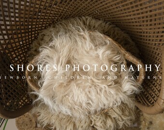 Op de afbeelding: Een witte nep bont prop voor newborn fotografie, geplaatst in een bruine rieten stoel. De tekst "SHORES PHOTOGRAPHY NEWBORN CHILDREN AND MATERNITY" is zichtbaar in de afbeelding.