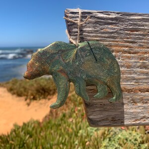 Puede incluir: Adorno de oso verde con purpurina sobre un fondo de madera marr&oacute;n r&uacute;stico. El oso est&aacute; colgado de una cuerda de yute.
