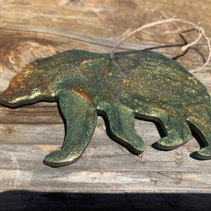 Puede incluir: Un adorno de oso de purpurina verde y dorada con un colgador de cuerda.