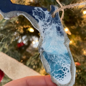 May include: A blue and white resin ornament shaped like the state of Florida. The ornament has a white wave design and a glittery finish.