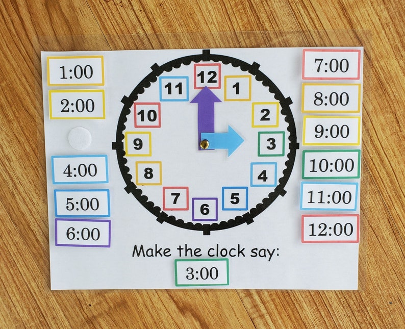 May include: A colorful clock face with movable hands. The clock face has numbers 1 through 12 in colorful squares. The hands are purple and blue. There are separate squares with the times 1:00 through 12:00. The text "Make the clock say: 3:00" is below the clock face.