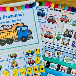 Puede incluir: Un archivador de aprendizaje preescolar con una ilustración de un camión volquete amarillo y el texto My Preschool Learning Binder, junto a hojas de actividades para emparejar colores, números y transportes, decorado con una guirnalda de bolas de fieltro.