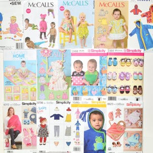 May include: A collection of twelve sewing pattern envelopes for infants and children, featuring various designs including hooded robes, dresses, bibs, booties, and baby gear. Each envelope displays colorful illustrations and photographs of finished garments.
