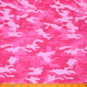 Op de afbeelding: Roze camouflage stof met een liniaal langs de onderkant. De stof heeft een patroon van verschillende roze tinten, waardoor een militair geïnspireerd ontwerp ontstaat. De liniaal toont metingen in centimeters.