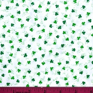 May include: White fabric with a repeating pattern of green shamrocks. The fabric is measured with a ruler in inches.