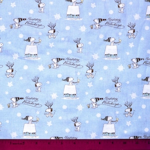 May include: Light blue fabric with a repeating pattern of Snoopy characters in winter attire, snowflakes, and the words "Happy Holidays" in a script font. The Snoopy characters are in black and white.