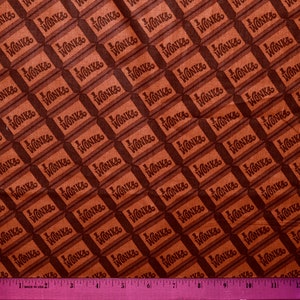 Puede incluir: Una tela marrón y naranja con un patrón repetido de barras de chocolate que dicen "Wonka" en ellas.
