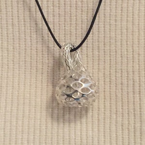 Op de afbeelding: Een zilveren ketting met een geometrische, opengewerkte hanger. De hanger heeft de vorm van een traan en hangt aan een zwart koord.