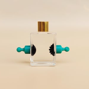 May include: A clear glass bottle with a gold lid and two black and teal bottle stoppers.