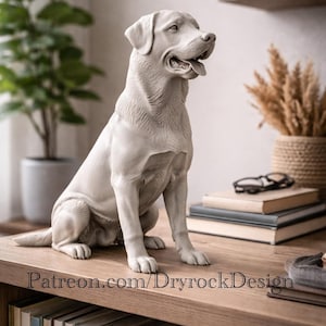 May include: A light gray Labrador Retriever statue in a seated position, with its tongue slightly out. The sculpture is placed on a wooden surface, with books, glasses, and decorative items in the background. The text "Patreon.com/DryrockDesign" is visible.