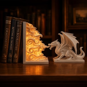Puede incluir: Una figura de dragón blanco con las alas extendidas y un sujetalibros a juego que emite una luz cálida y brillante. El sujetalibros tiene forma de explosión de fuego. Se ven tres libros antiguos.