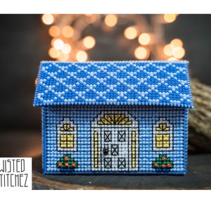 May include: A blue and white cross-stitch house with a yellow door and windows. The house is a small, decorative item.