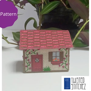 May include: A pink and brown cross-stitch house with a red door, a window with orange flowers, and green vines. The house is on a white background. PDF Pattern.