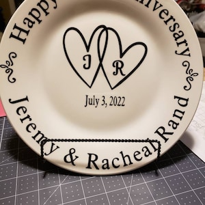 May include: White ceramic plate with black lettering that reads "Happy 12th Anniversary" and "Jeremy & Racheal" with two intertwined hearts and the initials "J" and "R" inside. The date "July 3, 2022" is printed below the hearts.