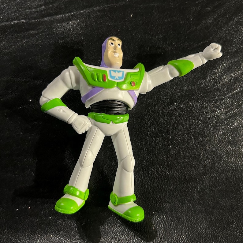 May include: A Buzz Lightyear action figure in a dynamic pose. The figure is mainly white with green and purple accents, including a green chest plate and accents on the arms and legs. The figure has a smiling expression and is posed with one arm raised.