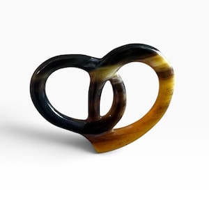 Könnte beinhalten: Ein glattes, poliertes Horn-Accessoire in Brezelform mit einem Farbverlauf von tiefem Schwarz und Dunkelbraun bis hin zu durchscheinenden Bernstein- und Goldgelbtönen, mit geschwungenem, geschlungenem Design und glänzender Oberfläche.