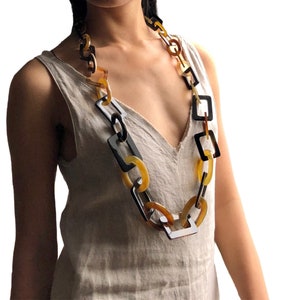 Könnte beinhalten: Eine lange Halskette aus großen, klobigen, braunen, schwarzen und gelben Kunststoffgliedern. Die Glieder sind quadratisch und rund.