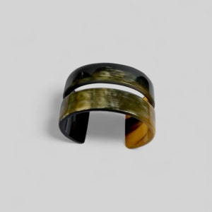 Pode incluir: Um bracelete largo de chifre preto e verde com um design de banda dupla. O bracelete é feito de chifre natural e tem um acabamento polido.