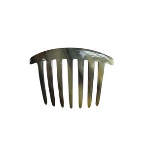 Pode incluir: Um pente de cabelo com uma superfície lisa e polida, apresentando um padrão marmoreado em tons de cinza translúcido, verde-oliva e castanho escuro. O pente possui uma borda superior curva e sete dentes cônicos espaçados uniformemente.