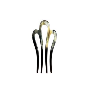 Peut inclure: Une fourche à cheveux à quatre dents, présentant une surface lisse et polie avec un motif marbré dans des tons noirs, gris et crème. Le design se compose d'une arche centrale reliant les dents, créant une forme symétrique, allongée et incurvée.