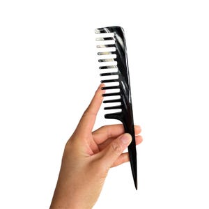 Peut inclure: Un peigne noir à dents larges avec un manche pointu. Le peigne a une finition brillante et est présenté sur un fond blanc. Les dents sont espacées uniformément. Le peigne semble être fait d'un matériau durable.