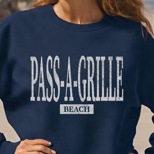 May include: A navy blue sweatshirt with the text "PASS-A-GRILLE BEACH" in white lettering.