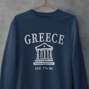Puede incluir: Una sudadera azul marino con un gráfico blanco de un edificio con columnas y el texto "GREECE EST. 776 BC".