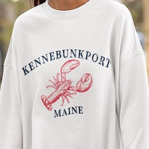 May include: White sweatshirt with a navy blue graphic of a lobster and the text "KENNEBUNKPORT MAINE".