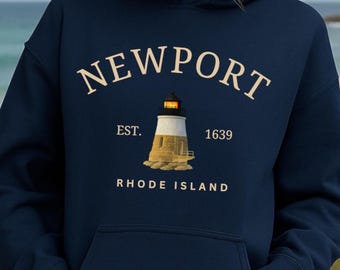 May include: Navy blue hooded sweatshirt featuring the word "NEWPORT" in a cream-colored, arched font. Below the word is a lighthouse illustration with the text "EST. 1639 RHODE ISLAND". The lighthouse is white and beige.