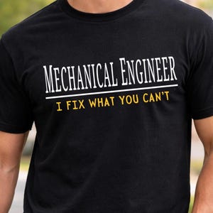 Könnte beinhalten: Schwarzes T-Shirt mit dem Text "MECHANICAL ENGINEER" in Weiß, unterstrichen mit Weiß, und dem Text "I FIX WHAT YOU CAN'T" in Gelb. Das Shirt ist aus einem weichen Material.