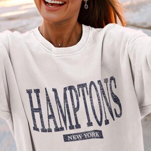 May include: White sweatshirt with a navy blue graphic that says "HAMPTONS NEW YORK".