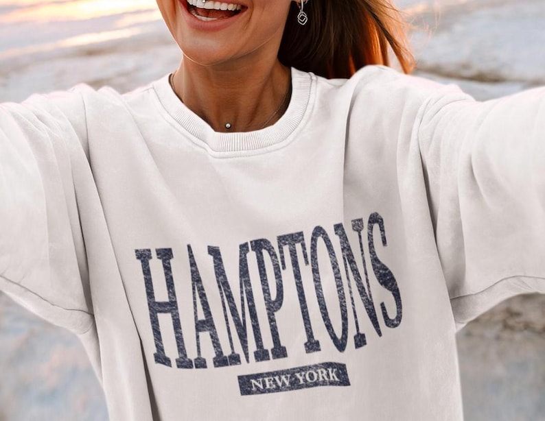 May include: White sweatshirt with a navy blue graphic that says "HAMPTONS NEW YORK".
