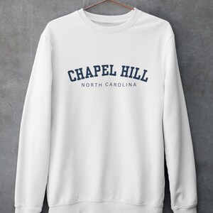 Puede incluir: Sudadera blanca con un dise&ntilde;o de arco azul marino que dice "Chapel Hill North Carolina".