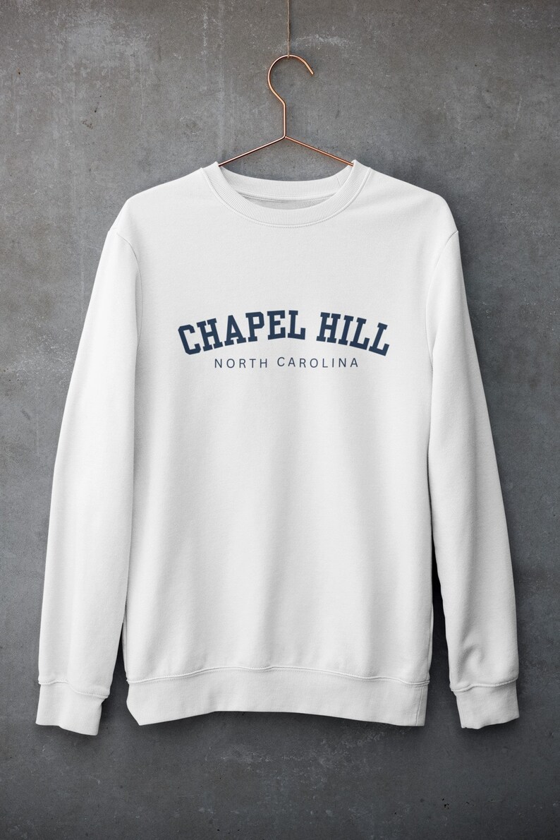 Puede incluir: Sudadera blanca con un dise&ntilde;o de arco azul marino que dice "Chapel Hill North Carolina".
