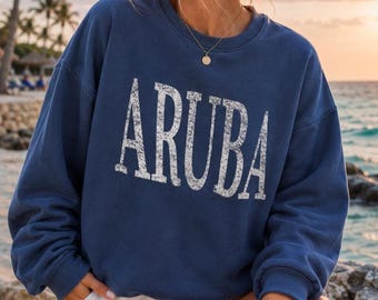 May include: A navy blue crewneck sweatshirt featuring the word ARUBA printed in large, white, distressed capital letters across the chest. The garment has long sleeves, a ribbed neckline, and a relaxed fit, providing a casual look.
