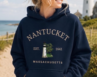 Könnte beinhalten: Ein marineblauer Kapuzenpullover mit dem Text NANTUCKET in geschwungener beiger Schrift über einer Grafik eines weißen Leuchtturms mit grünen Bäumen. Der Text EST. 1641 steht beidseitig des Leuchtturms, darunter steht MASSACHUSETTS.