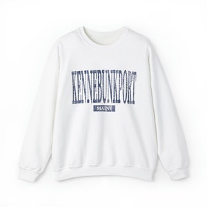 K&ouml;nnte beinhalten: Ein wei&szlig;es Sweatshirt mit Rundhalsausschnitt und dem Text "KENNEBUNKPORT" in verblichenen marineblauen Buchstaben auf der Brust. Darunter befindet sich ein kleineres Rechteck mit dem Wort "MAINE" in Marineblau. Das Sweatshirt hat lange &Auml;rmel.