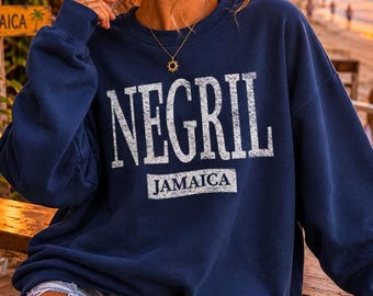 May include: A navy blue crewneck sweatshirt featuring the word NEGRIL in large, distressed white capital letters, with the word JAMAICA printed in a smaller white rectangular box directly underneath the main text on the front of the garment.