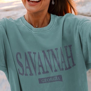 K&ouml;nnte beinhalten: Ein blaugr&uuml;ner Pullover mit dem Aufdruck "SAVANNAH GEORGIA" in dunkelblau.